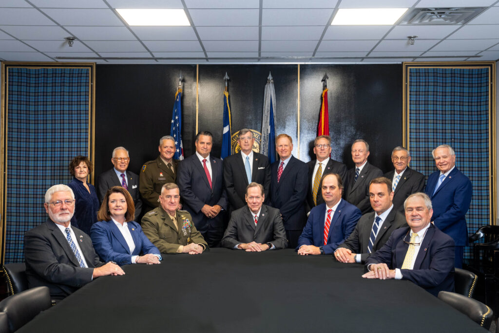 Formal group portrait of The Citadel Board of Visitors, with members seated at a conference table and others standing behind them, posed in a meeting room.