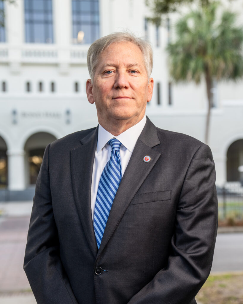 Professional headshot of James Nicholson in a black suit and blue striped tie standing outdoors at The Citadel.