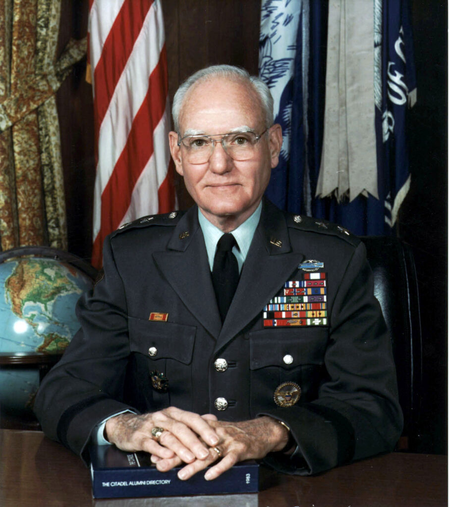 Portrait of a U.S. Army general in dress uniform seated at a desk with American and South Carolina flags behind him.