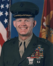 Portrait of a U.S. Marine Corps general in dress uniform standing in front of military flags.