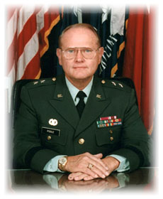 Portrait of a U.S. Army officer in dress uniform seated in front of military flags.