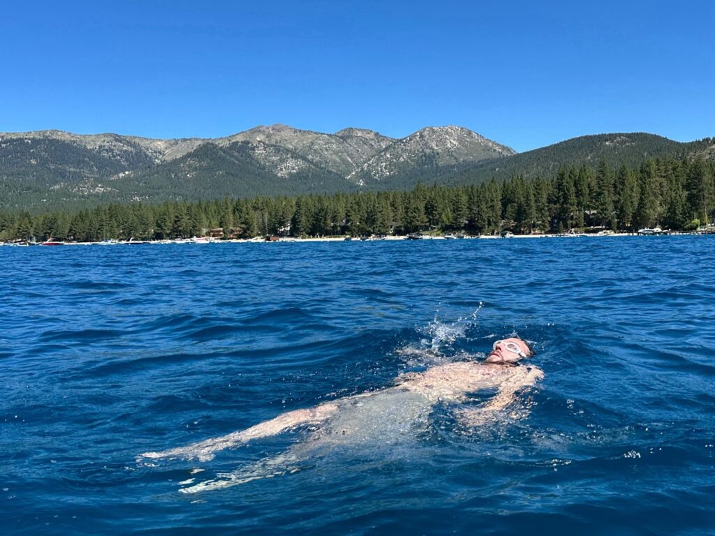 Swimmer floating on his back in Lake Tahoe with forested mountains along the shoreline.