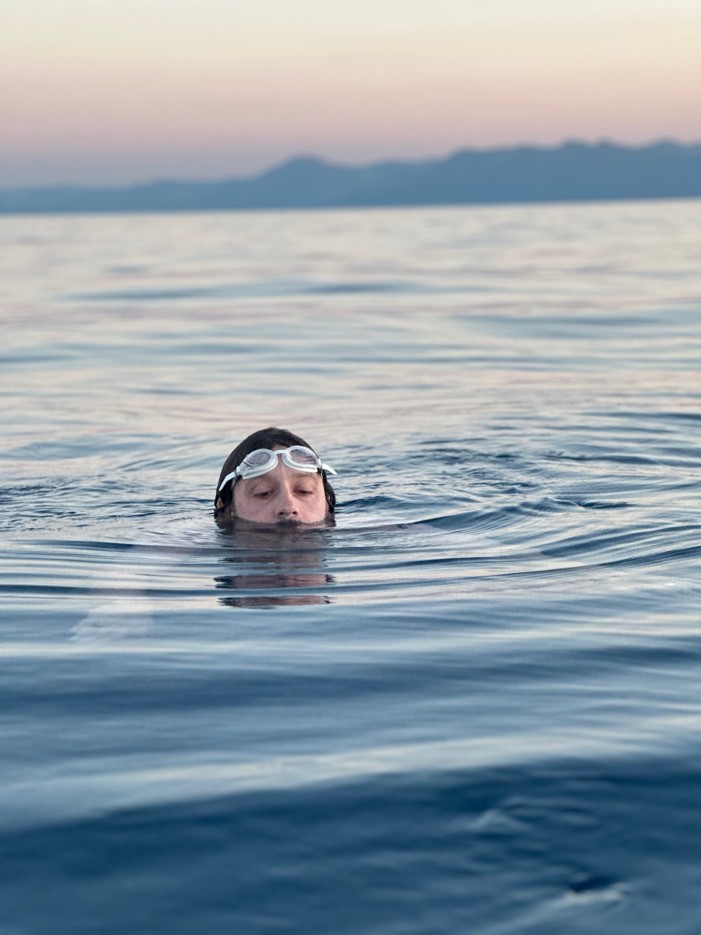Swimmer wearing goggles in Lake Tahoe with mountains in the distance.
