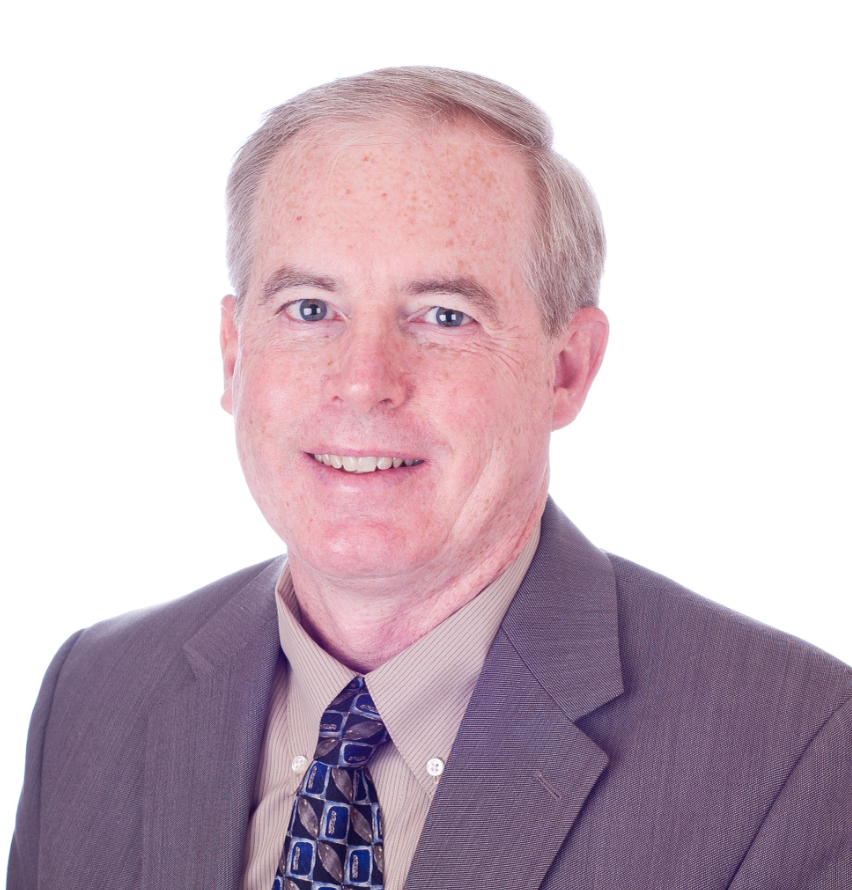 Headshot of Carlos Coe in a gray suit and patterned tie, smiling against a light gray background.
