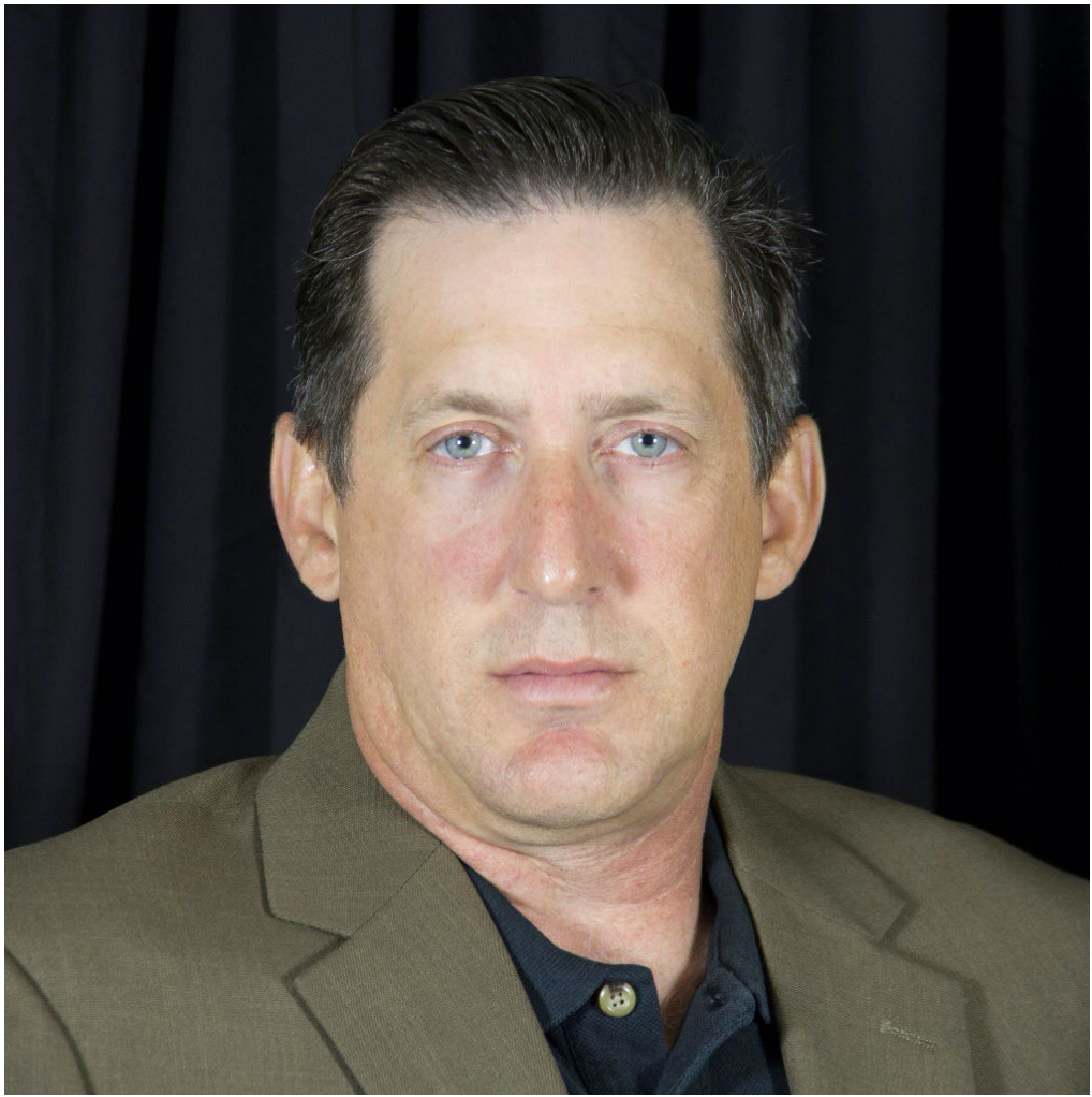 Portrait of Dr. Eric Bailey in a blazer and collared shirt, facing the camera against a dark backdrop.