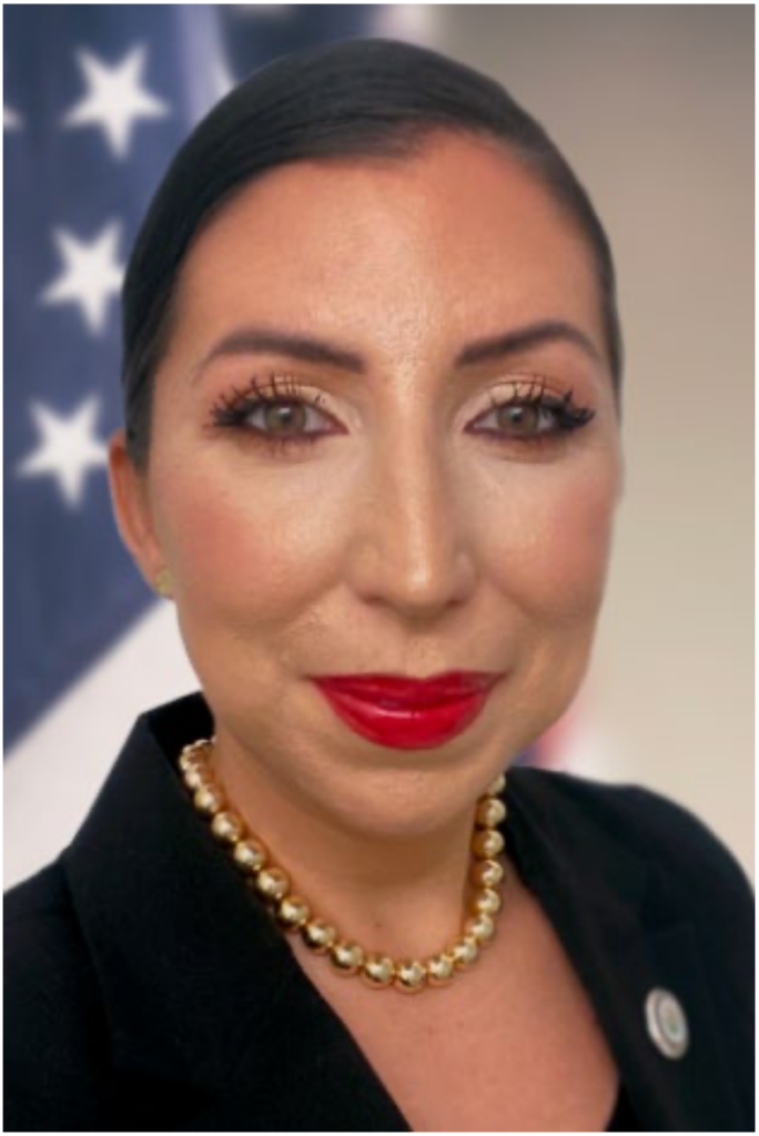 Portrait of Maj Sandra Wright wearing a black blazer and pearl necklace, with an American flag in the background.
