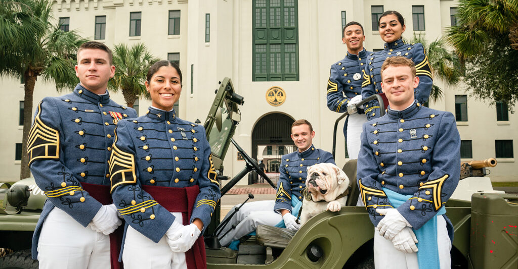 Cadets with a bulldog in a jeep in front of the Barracks.