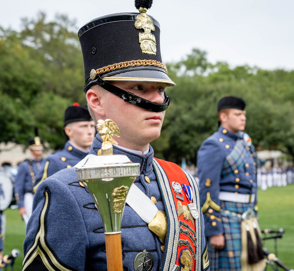 Citadel cadet in dress uniform holding a ceremonial mace during a parade.