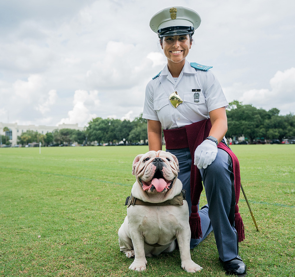 A cadet in a white dress uniform poses with The Citadel’s bulldog mascot on Summerall Field.