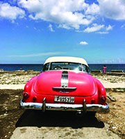 A photograph of a 1950's red convertible Pontiac on the beach in Havana.