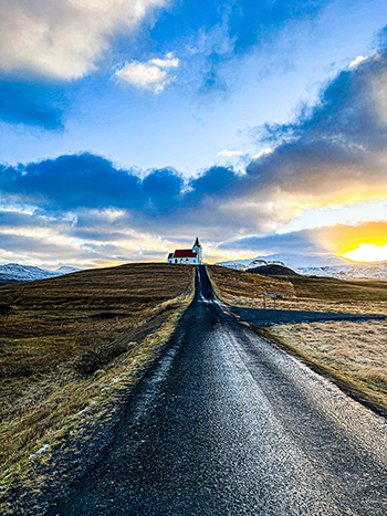 Photograph of a road with a small red church in the distance