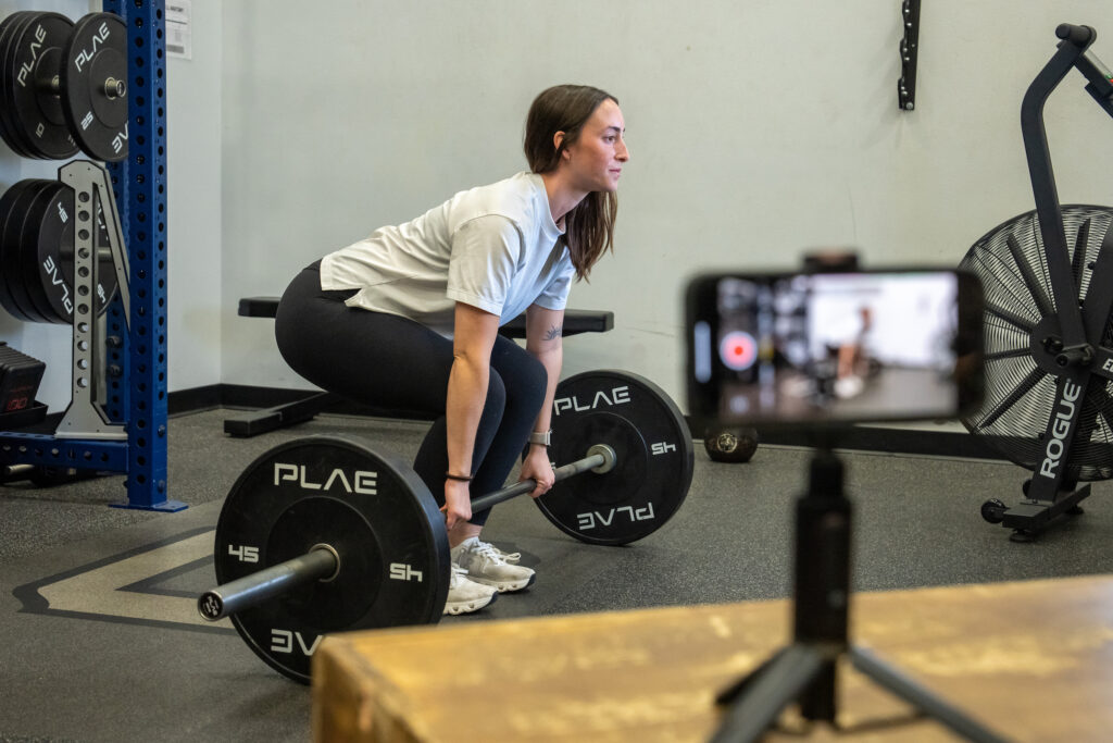 tudent performs a deadlift during a strength and conditioning exercise assessment, demonstrating applied coaching and performance analysis techniques.