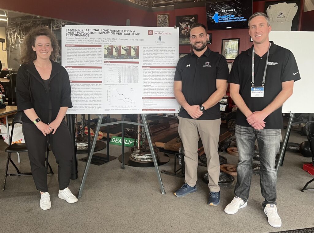 Researchers with a poster presenting findings on the impact of external load on vertical jump performance in cadets