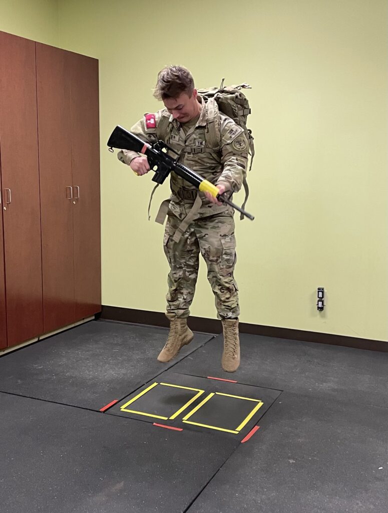 Citadel cadet completing a vertical jump test while carrying a military rucksack and equipment.