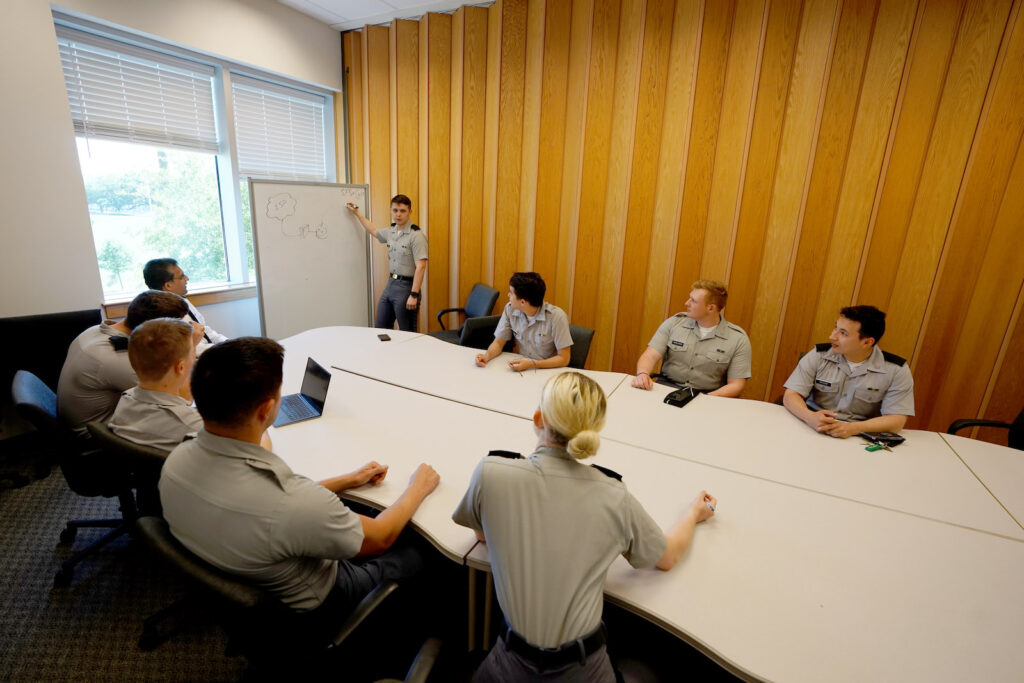 Citadel cadets participate in a group discussion as one cadet presents at a whiteboard.