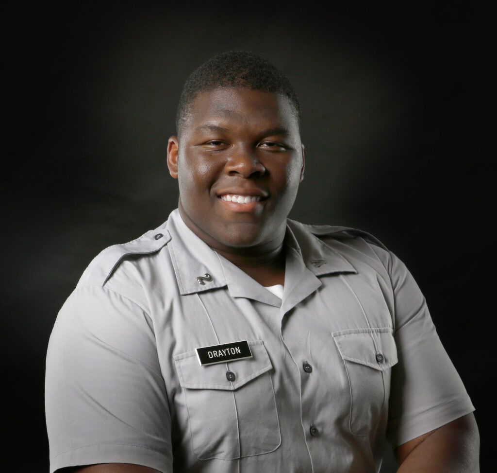 Smiling Citadel cadet Drayton in a gray uniform posed against a black background.