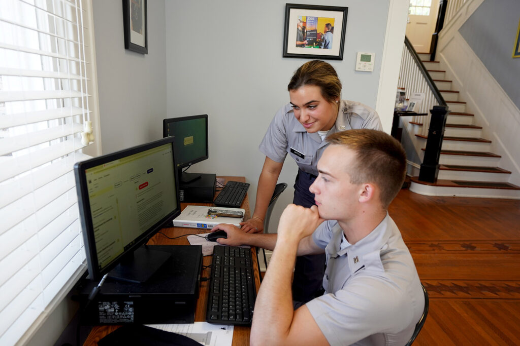 Two cadets work together at a desktop computer in an office.