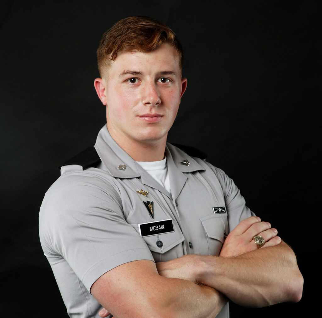 Cadet McBain poses in uniform with his arms crossed against a black background.