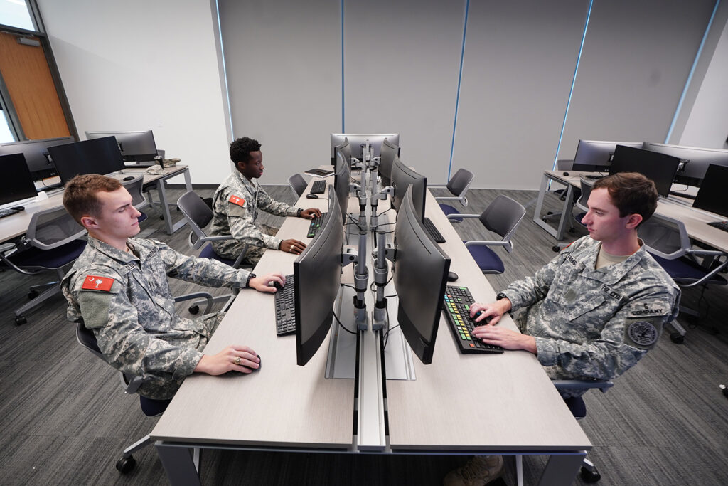 Three cadets work at computer stations in a technology lab.