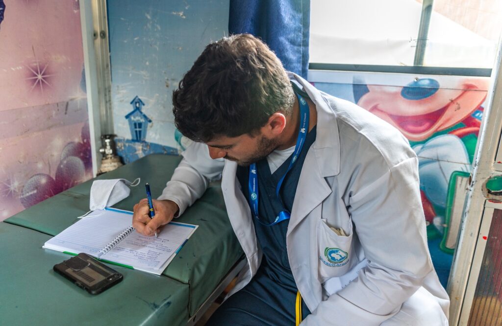 Medical volunteer in a white coat writes notes during a community health outreach activity.