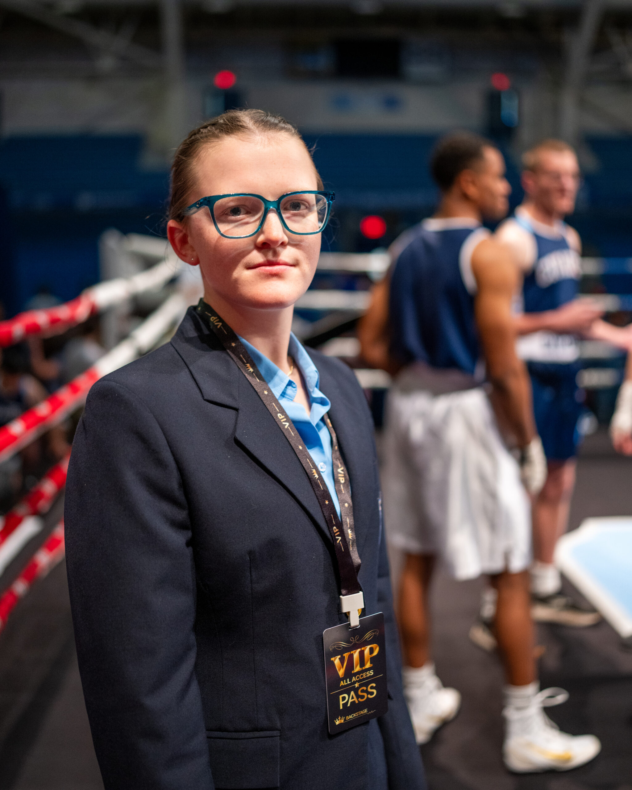 Cadet in business attire wearing a VIP credential stands ringside during a boxing match at The Citadel.