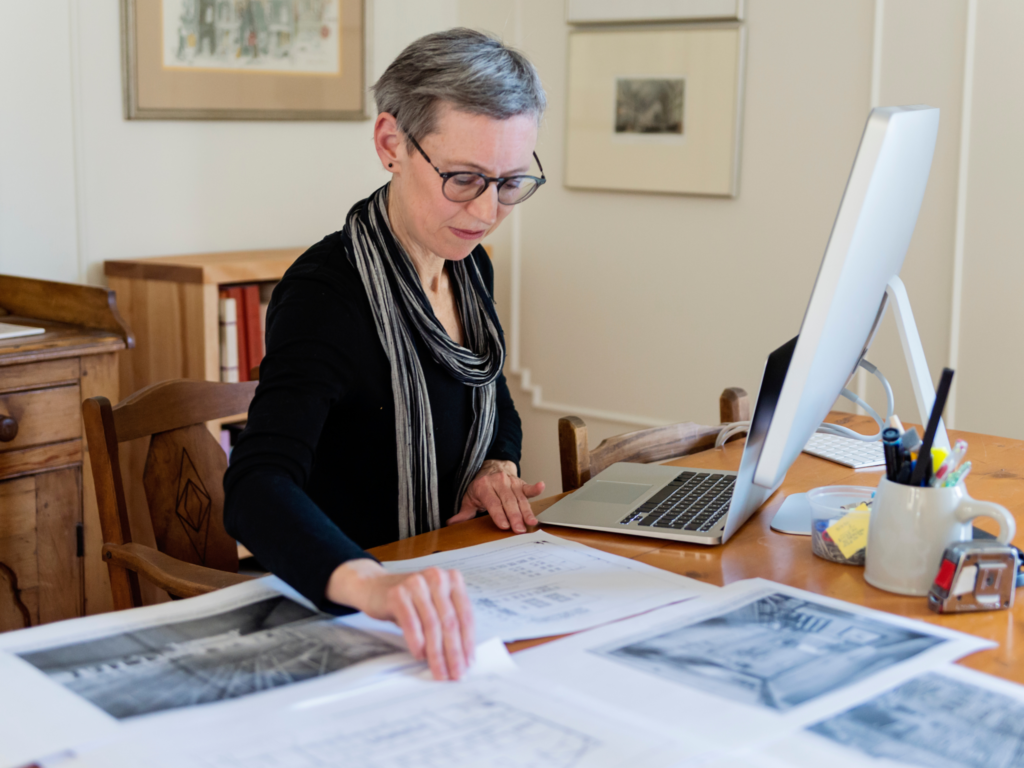 Woman reviewing historical photographs and documents while working at a computer.