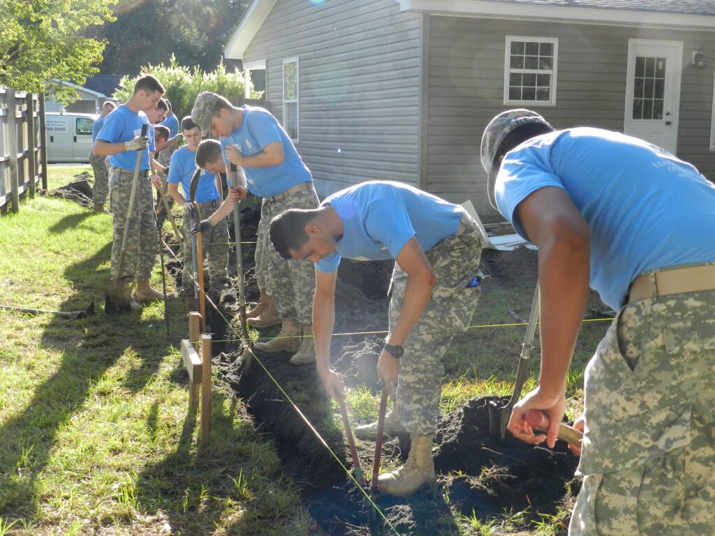 Citadel cadets dig a trench alongside a house during a community service project.