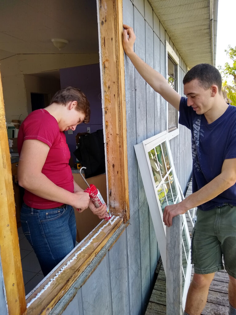 Two volunteers install a window during a home repair service project.