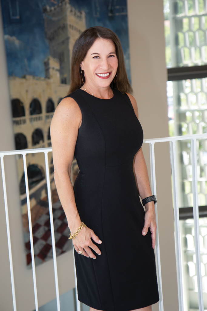 Woman in a black dress smiles for a professional portrait indoors.