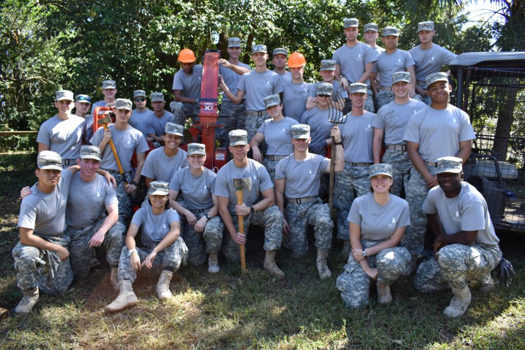 Group of Citadel cadets in camouflage uniforms posing with landscaping tools and equipment after an outdoor service project.