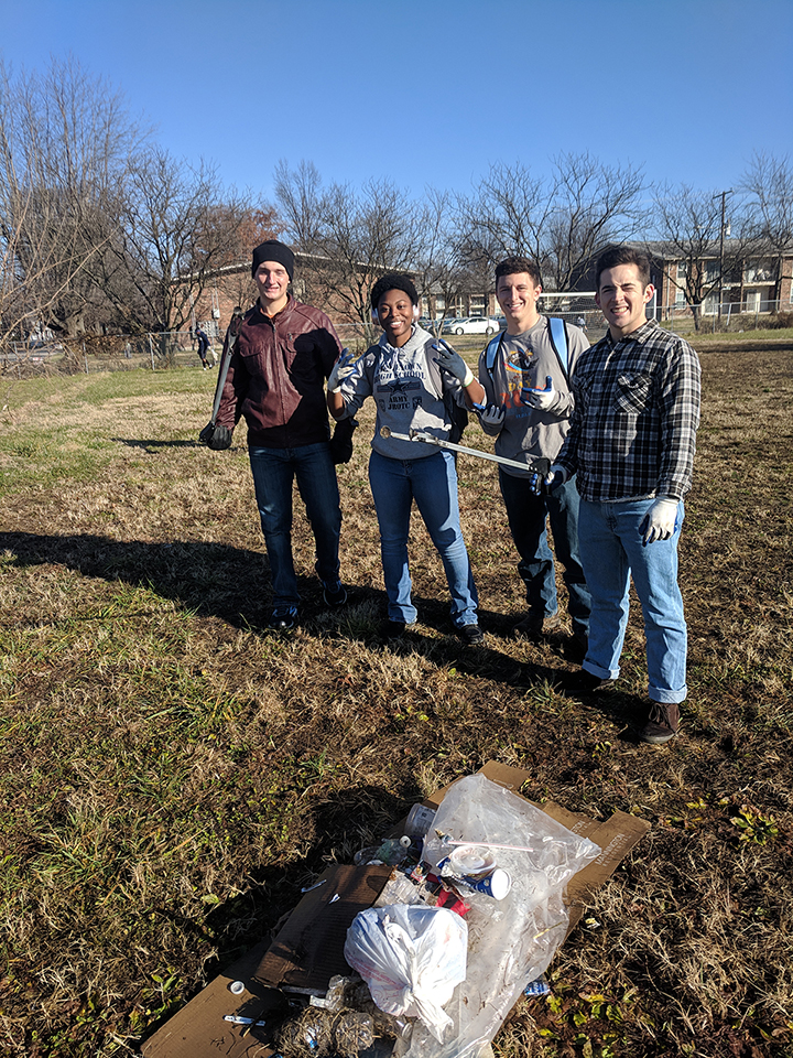 Four volunteers pose with cleanup tools and collected trash during a community service project.