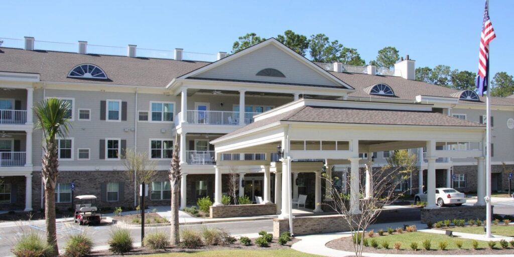 Exterior of a large residential community building with covered entrance, landscaped grounds and an American flag.