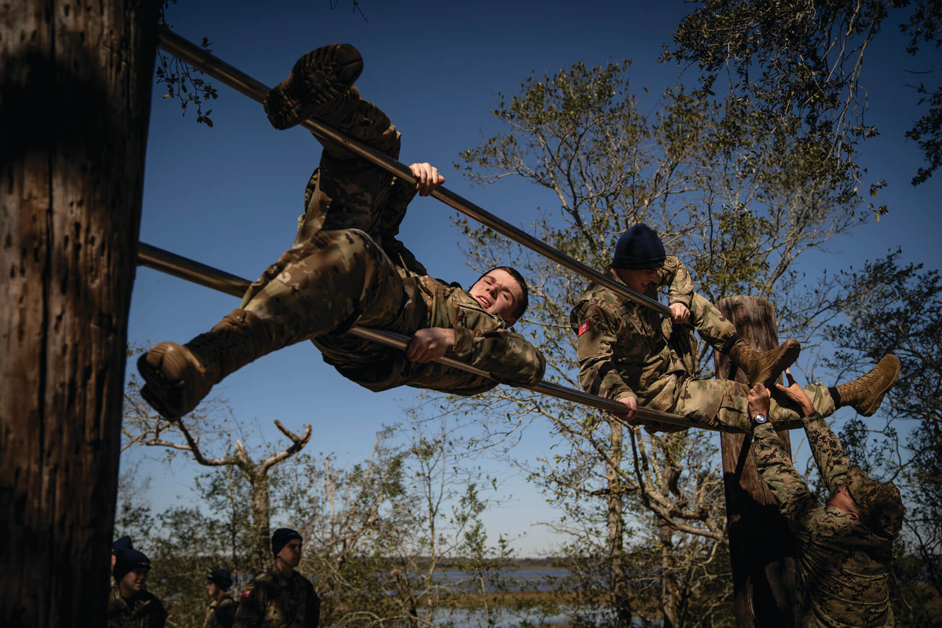 Military personnel navigating horizontal bars during an outdoor obstacle course.