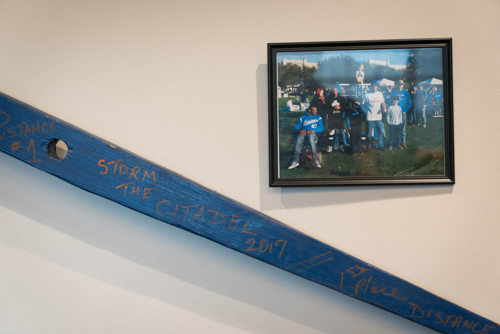 Blue wooden beam signed with “Storm the Citadel 2017” displayed beside a framed group photograph.