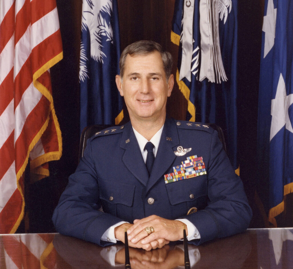Portrait of a U.S. Air Force general in uniform seated in front of American and South Carolina flags.