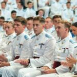 Cadets in dress white dress uniforms sit and applaud during an awards ceremony in McAlister Field House.