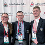 Cadets McKenna Magin, Dylan Horne and Banks Scarpa pose in front of an Alpha Epsilon Delta backdrop at the organization’s Centennial National Convention, wearing conference badges and Citadel blazers.