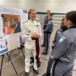 Standing in front of an academic poster, Cadet Lucy McArthur discusses her research with peers during the annual Academic Excellence Day event.