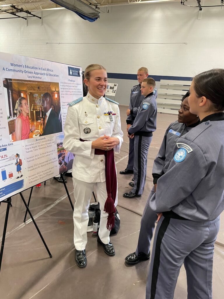 Standing in front of an academic poster, Cadet Lucy McArthur discusses her research with peers during the annual Academic Excellence Day event.