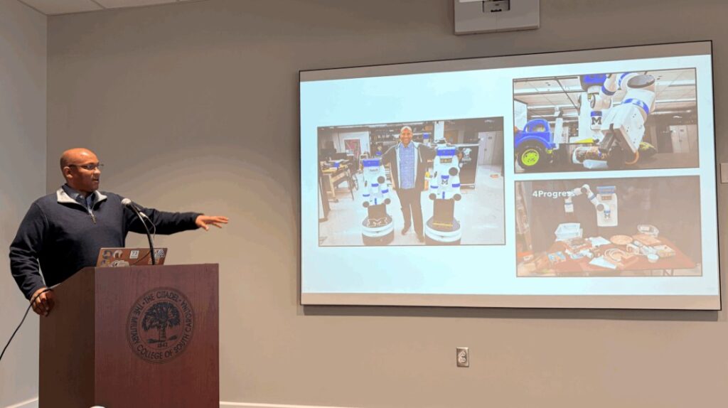 Odest Chadwicke Jenkins, Ph.D., University of Michigan robotics and computer science professor, stands behind a podium at the Swain Boating Center, pointing to a PowerPoint presentation as part of his lecture on semantic robot programming.