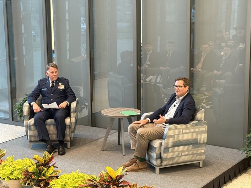 Baker School of Business Dean Michael R. Weeks, in uniform, sits onstage in an armchair as he facilitates a discussion with Isaac Morton, founder and CEO of Smithey Ironware Company, who is seated opposite him.