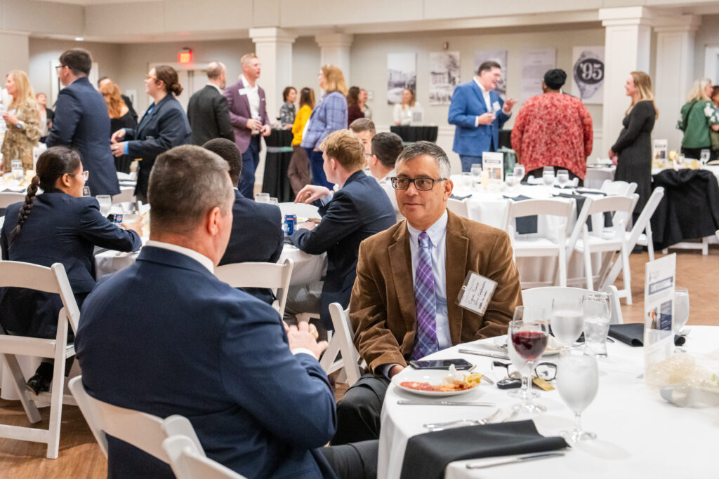 Guests in business attire dine and mingle at cloth-covered round tables during the Camo to Classroom event in the Holliday Alumni Center.