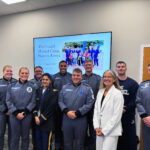 Retired Army Reserve Maj. Gen. Jami C. Shawley and Dr. Sarah Imam stand with cadets who participated in the Kenya Medical Camp, gathered in a classroom in front of a slide referencing the program in Kenya.