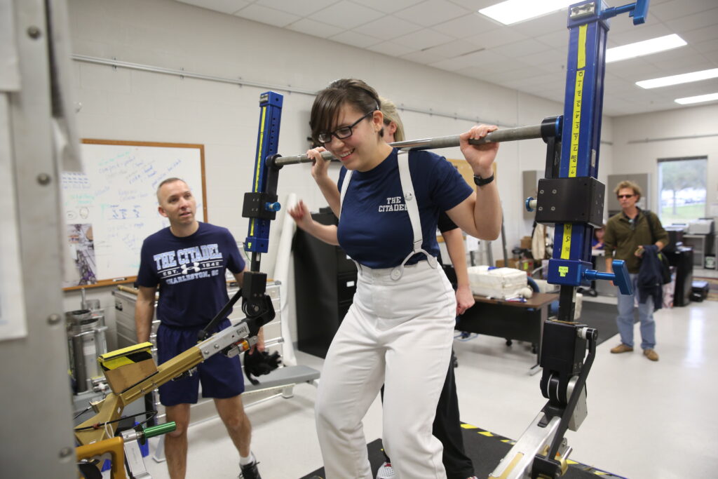 A Citadel cadet participates in a spaceflight equipment training exercise while Randy Bresnik observes nearby.