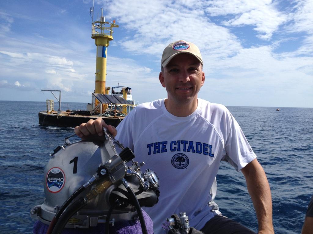 Randy Bresnik poses beside diving equipment at a NEEMO dive site while wearing a Citadel T-shirt.