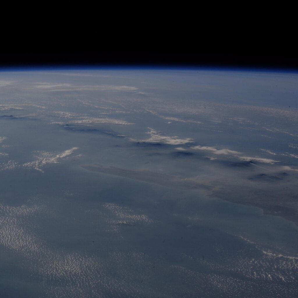 View from space of a mountain range beneath a hazy atmosphere and the dark horizon of space.
