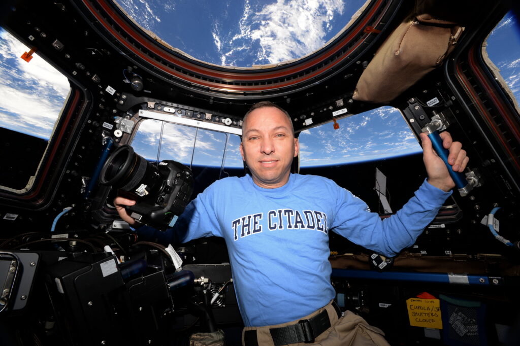 Randy Bresnik holds a camera inside the International Space Station’s cupola while wearing a blue Citadel shirt