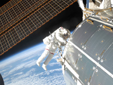 Astronaut Randy Bresnik performs a spacewalk outside the International Space Station with Earth visible below.