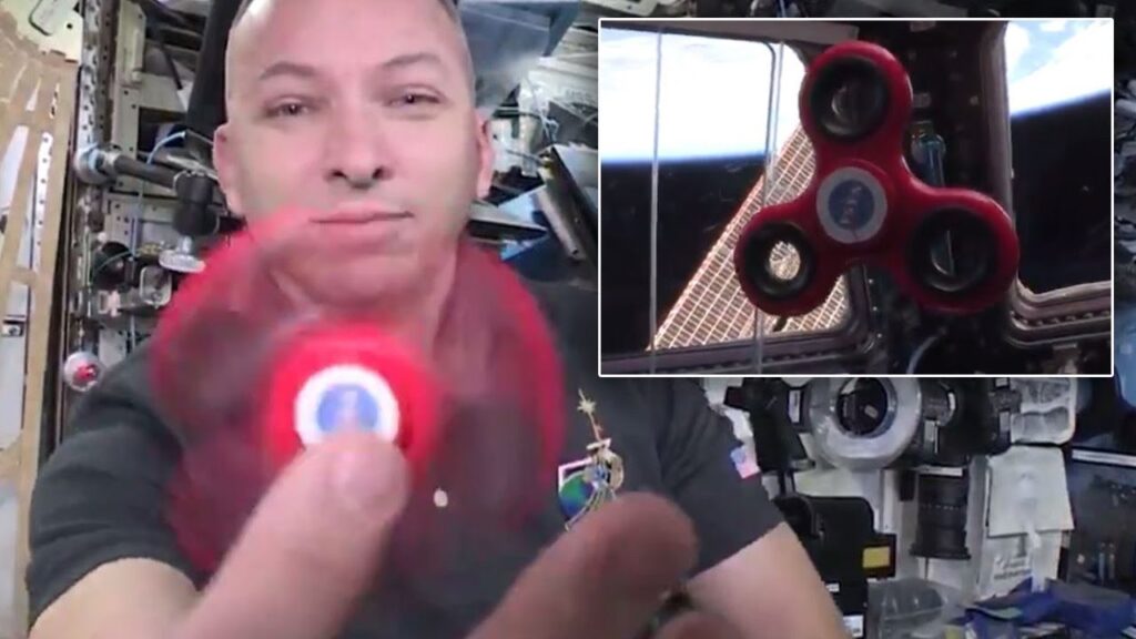 An astronaut demonstrates a spinning red fidget spinner aboard the International Space Station.