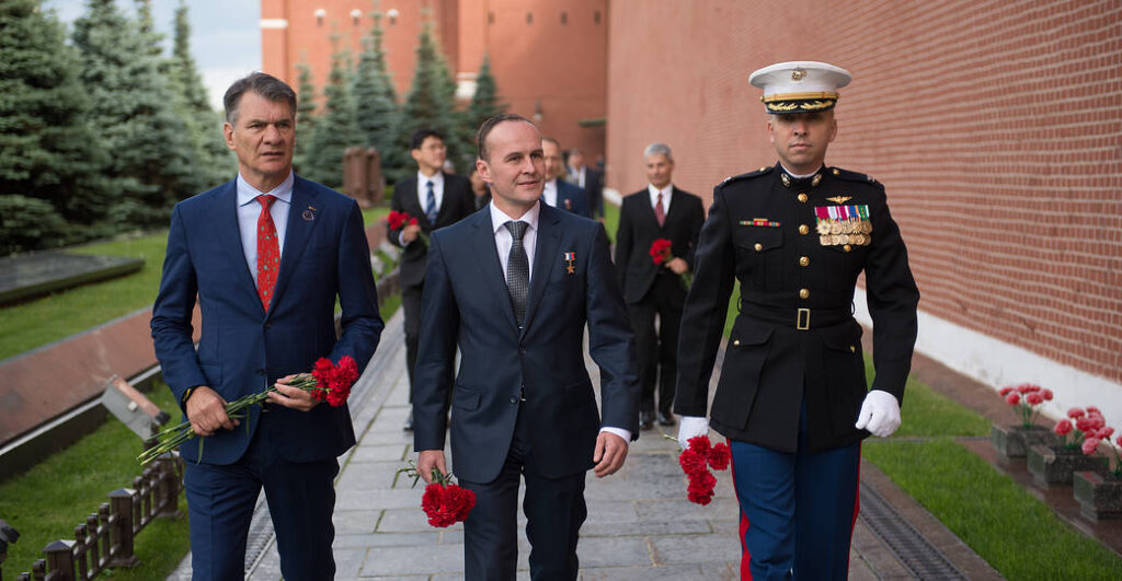 Three men, including a U.S. Marine, carry red flowers during a memorial ceremony.
